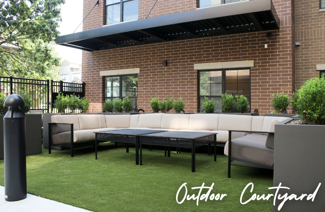 Outdoor courtyard with beige seating, black tables, and artificial turf in front of brick building.