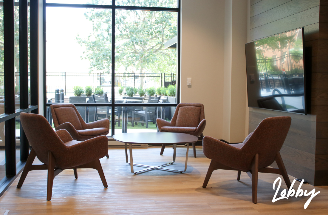 Cozy seating area with four brown chairs around a table, near a large window overlooking an outdoor patio.