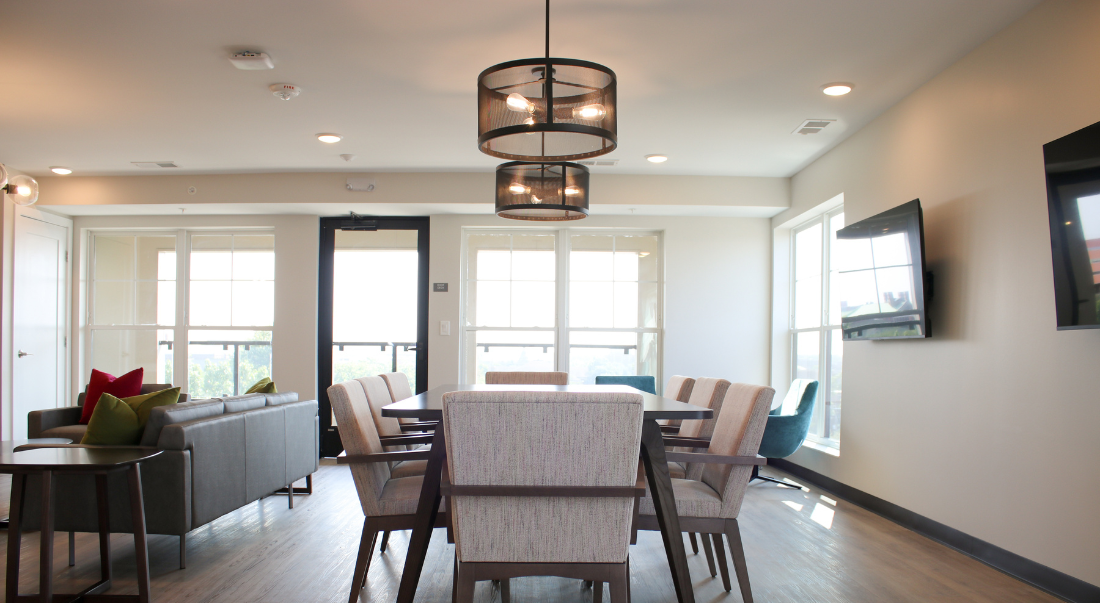 A modern lounge with a dining table, chairs, sofa, and a TV; neutral colors. 