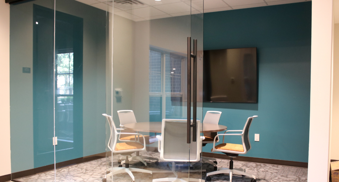 Group study room with glass walls, round table, chairs, TV, teal and white walls.