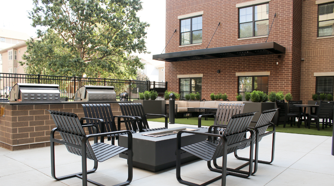 Outdoor courtyard with grills, seating around a fire pit, and brick building backdrop.