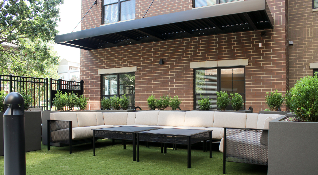 Outdoor courtyard with beige sectional sofa, black tables, and artificial grass.