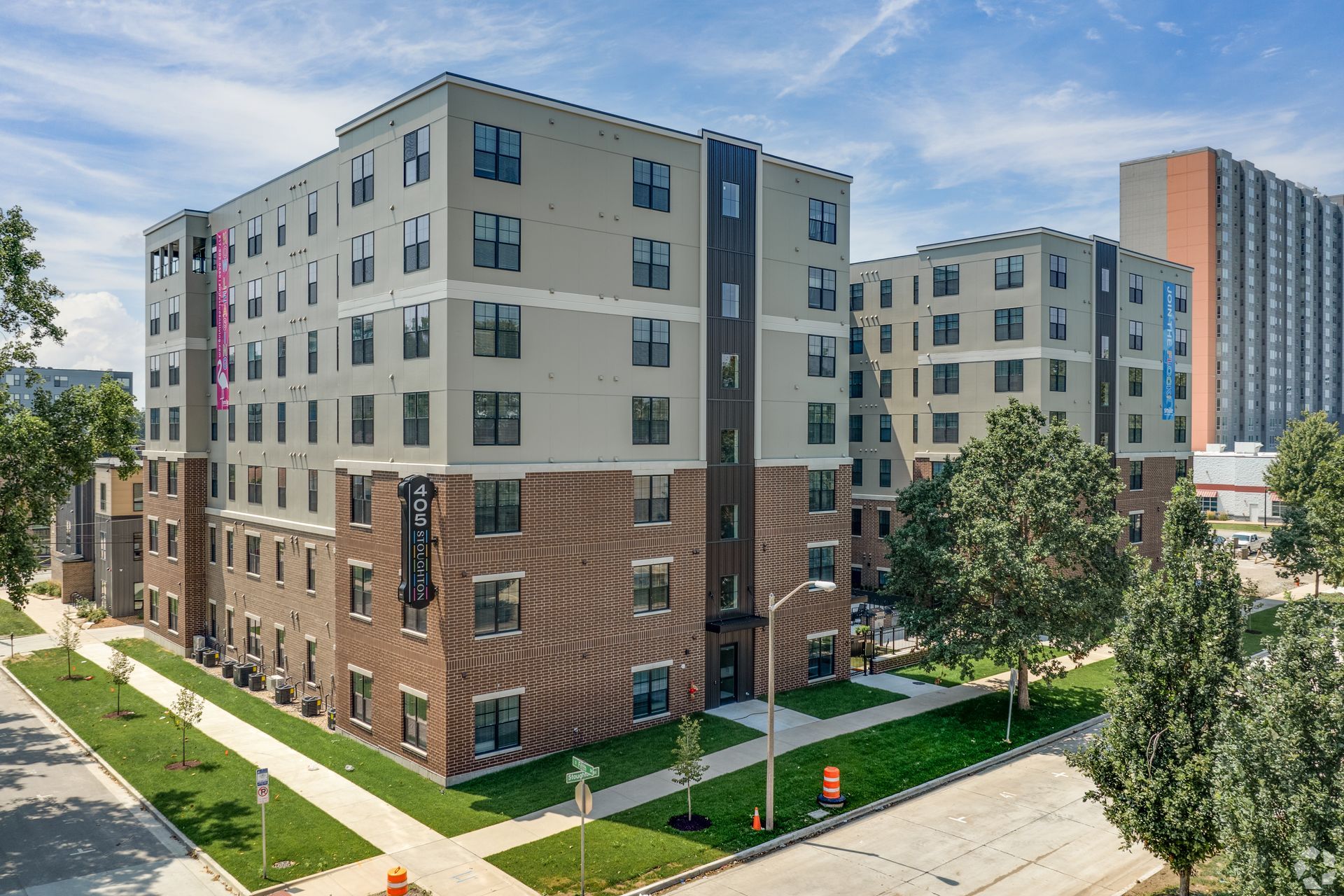 Modern multi-story apartment buildings with brick and gray exteriors under a blue sky.