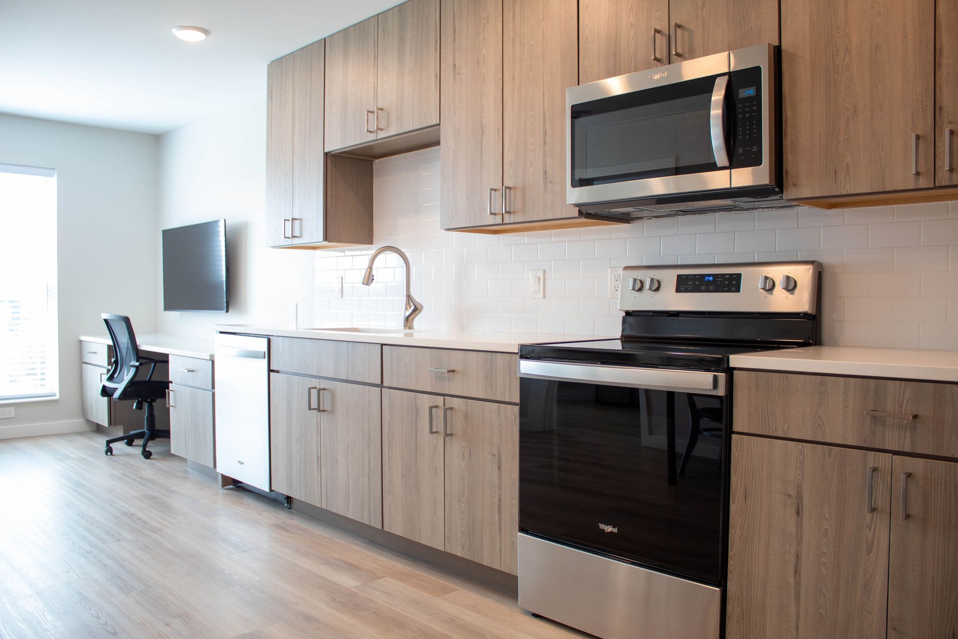 Modern kitchen with light wood cabinets, stainless steel appliances, and a window.