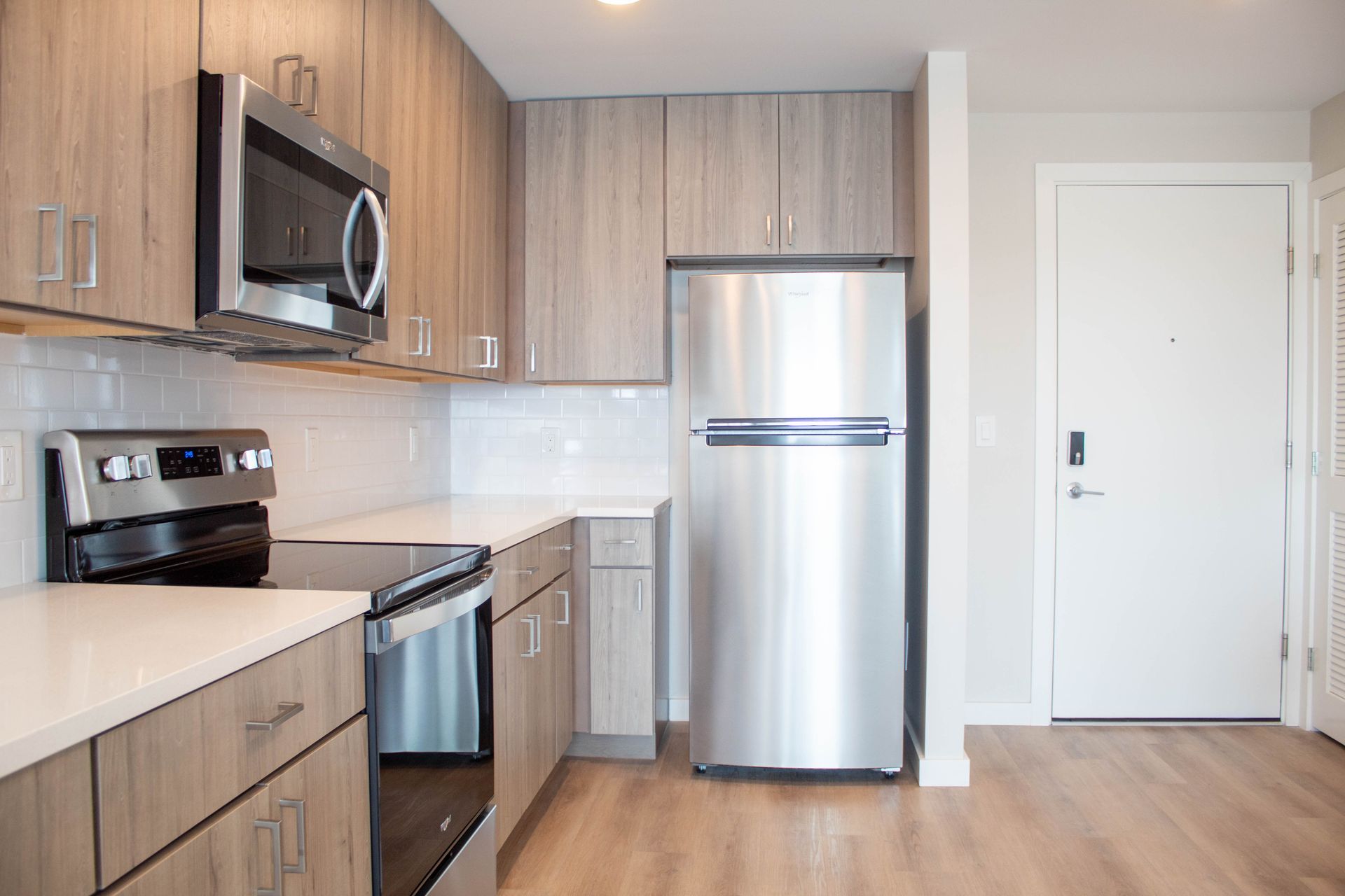 Modern kitchen with light wood cabinets, stainless steel appliances, and white countertops.