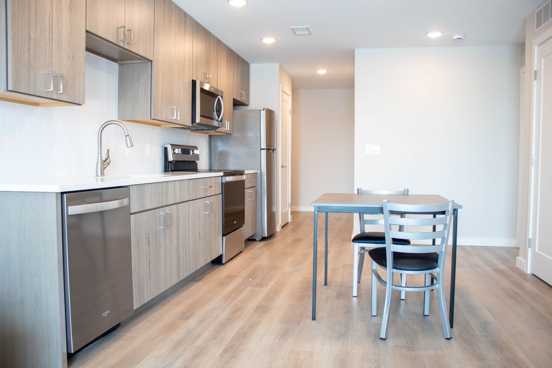 Modern kitchen with stainless steel appliances, light wood cabinets, and dining table.