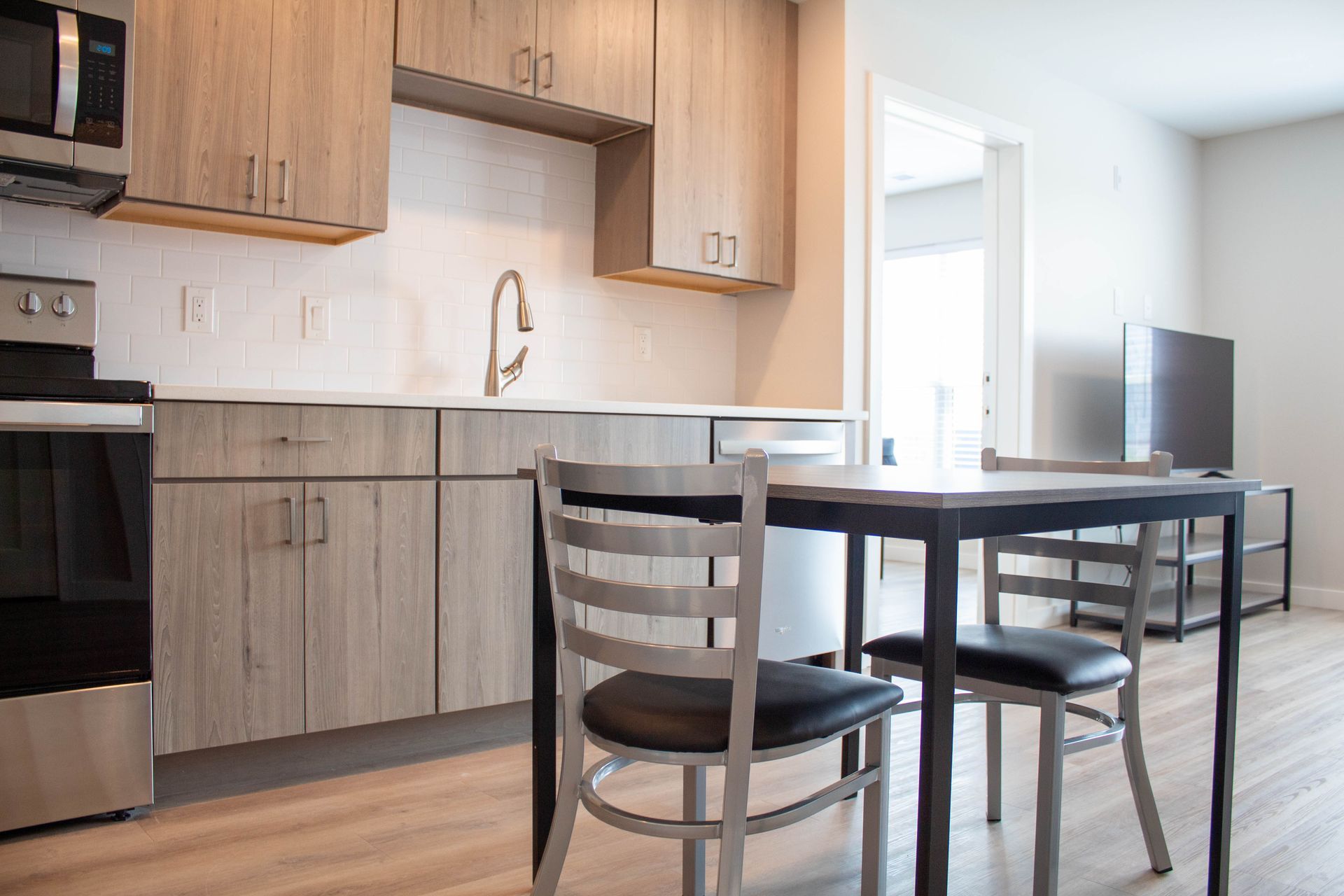 Small kitchen with wooden cabinets, stainless steel appliances, table with chairs, and television.