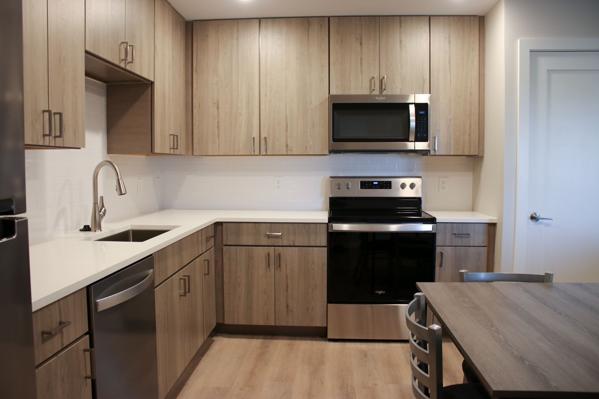 Modern kitchen with light wood cabinets, white countertops, and stainless steel appliances.