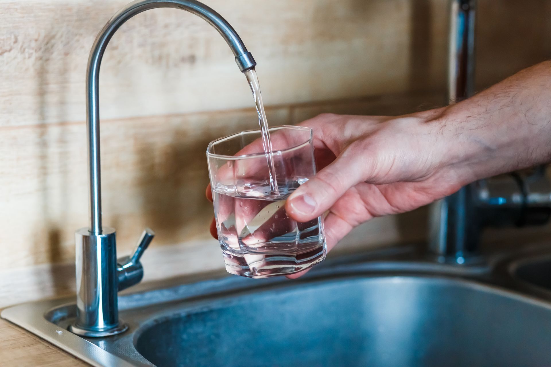 A person is pouring water into a glass from a faucet.