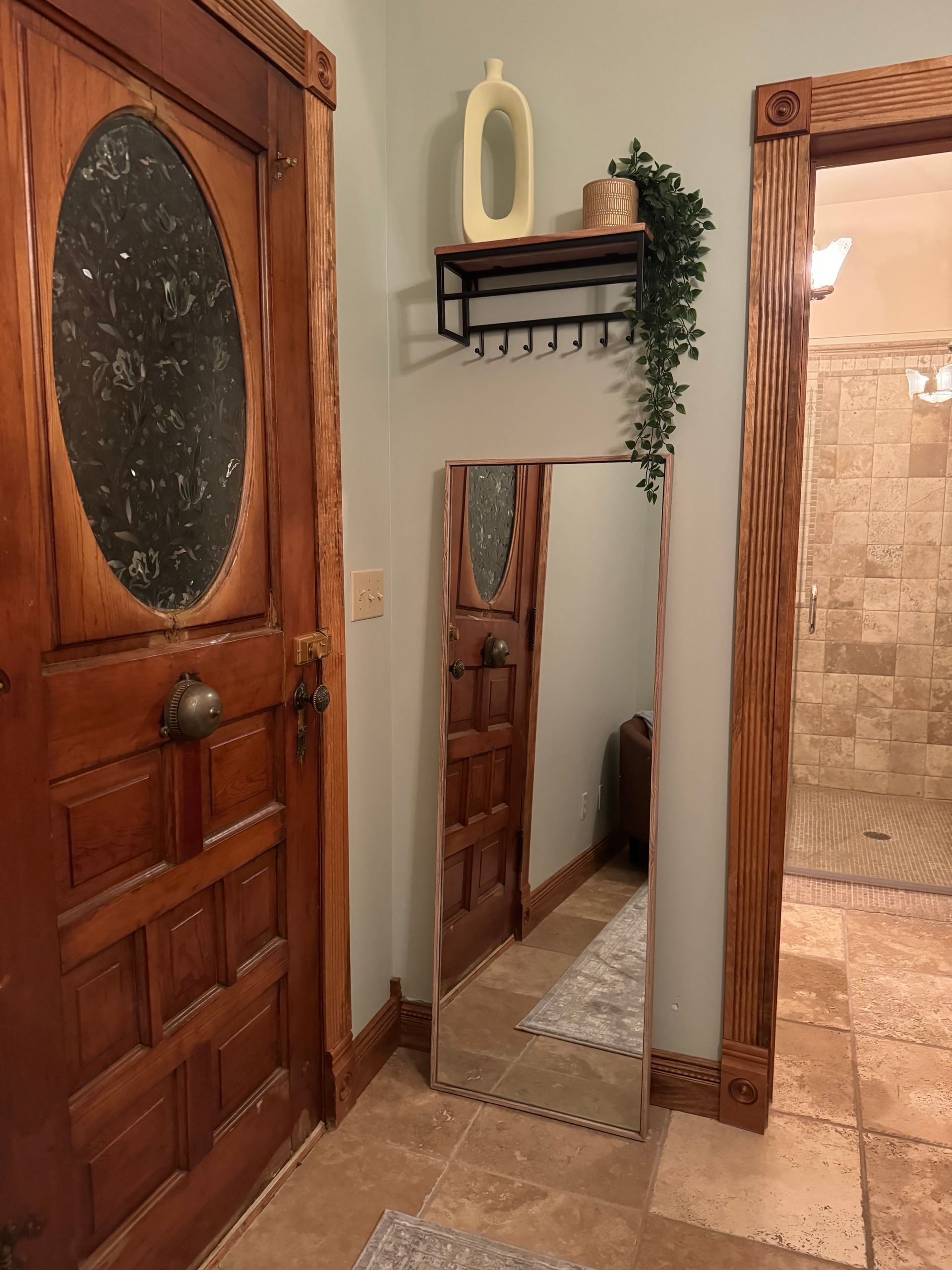 A hallway with a mirror and a wooden door leading to a bathroom.