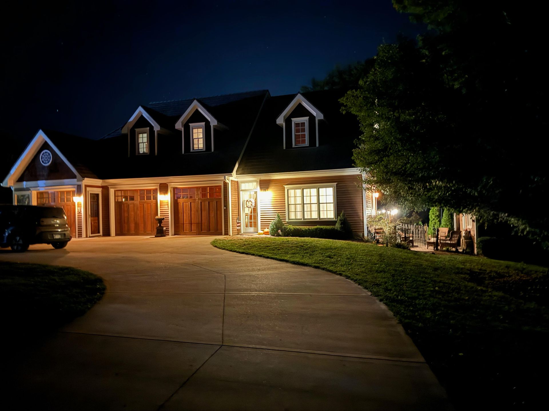A large house is lit up at night with a car parked in front of it.