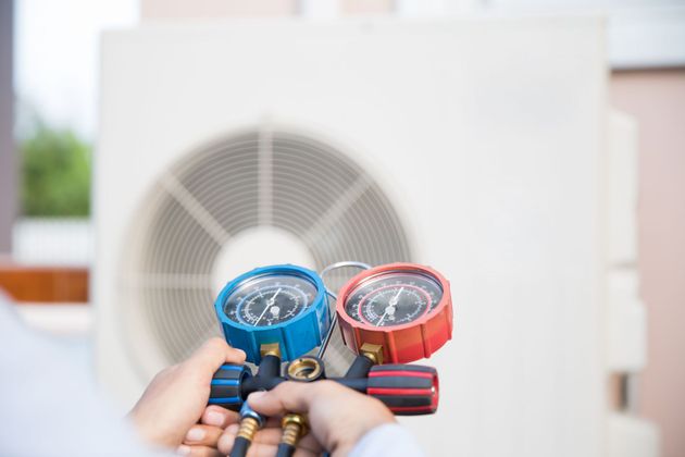 A person is holding two gauges in front of an air conditioner.