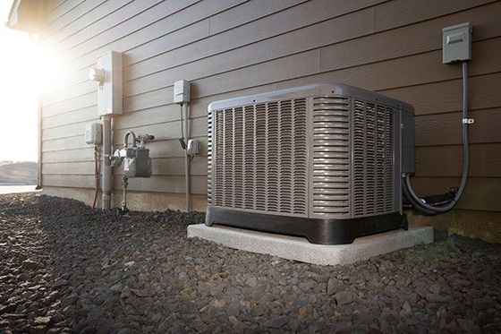 Air conditioning unit outside a brown house, gravel ground, sunny day.