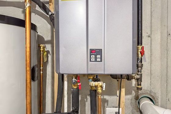 Tankless water heater and water tank in a basement. Copper pipes, gray appliance, and red valves.