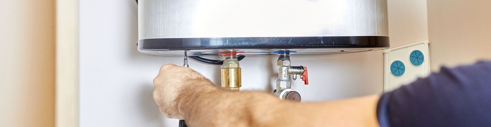 Person adjusts valves on a water heater, likely for maintenance. They're indoors, near white walls.