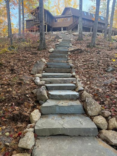 Stone steps leading up to a large cabin in a wooded area with fall foliage.