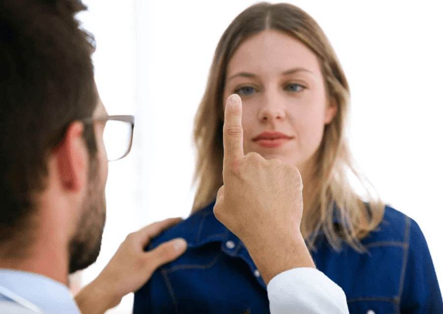 Doctor pointing finger, testing patient's eye movement in a brightly lit room. Woman looks forward.