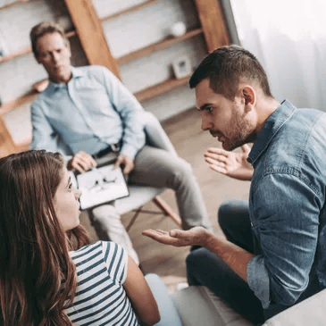 Couple arguing in therapy session; therapist observes.