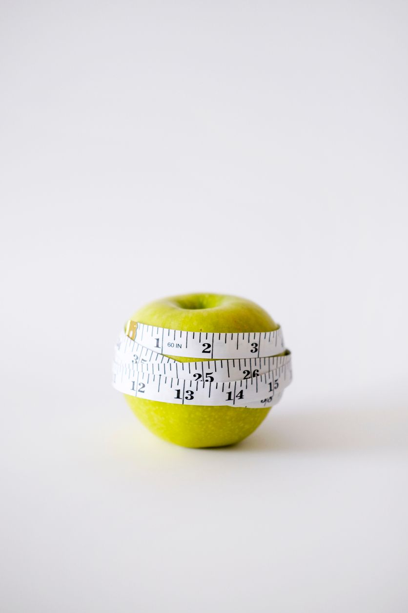 Green apple wrapped with white measuring tape.