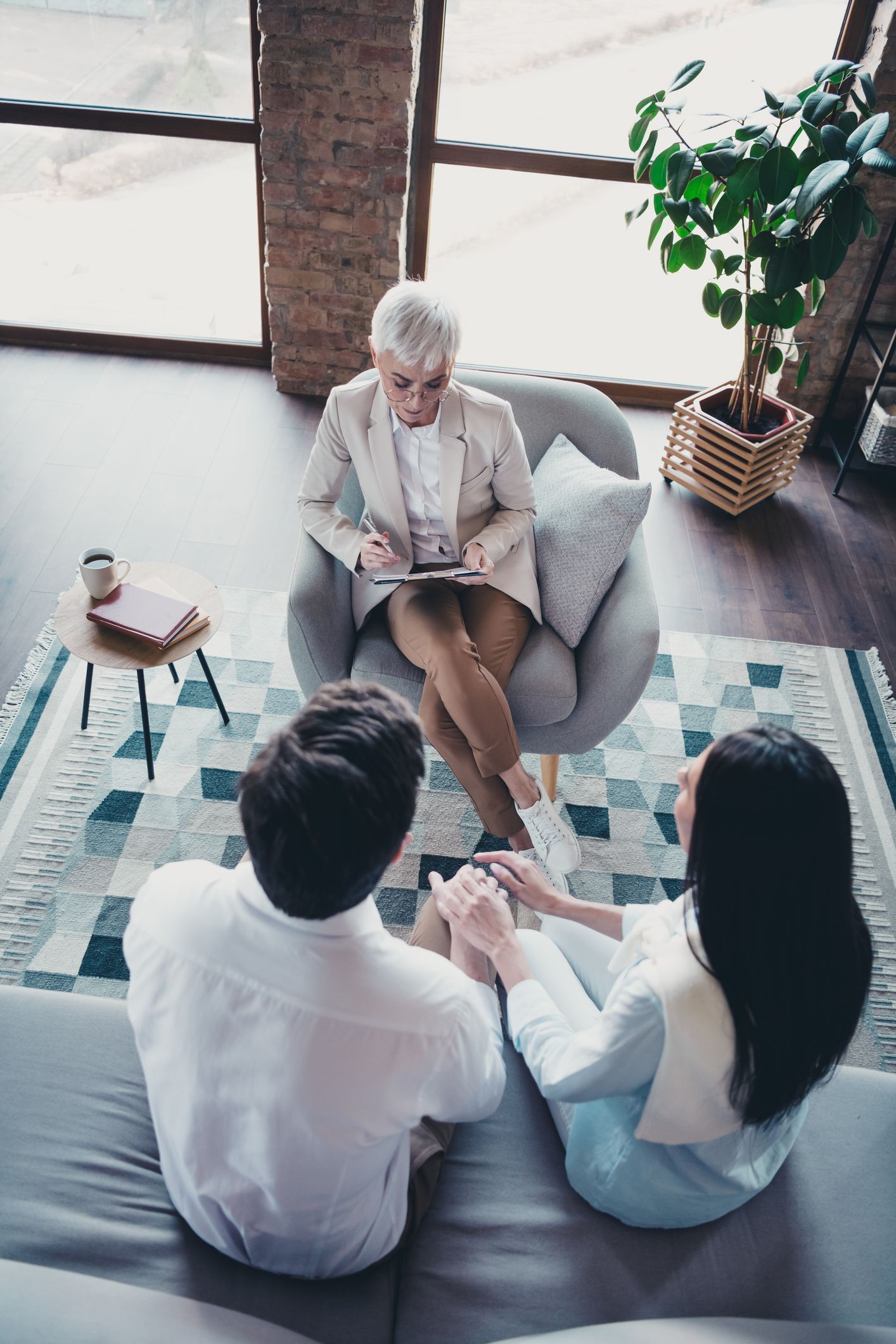 Couple seated on sofa in therapy session with therapist seated in armchair, taking notes.
