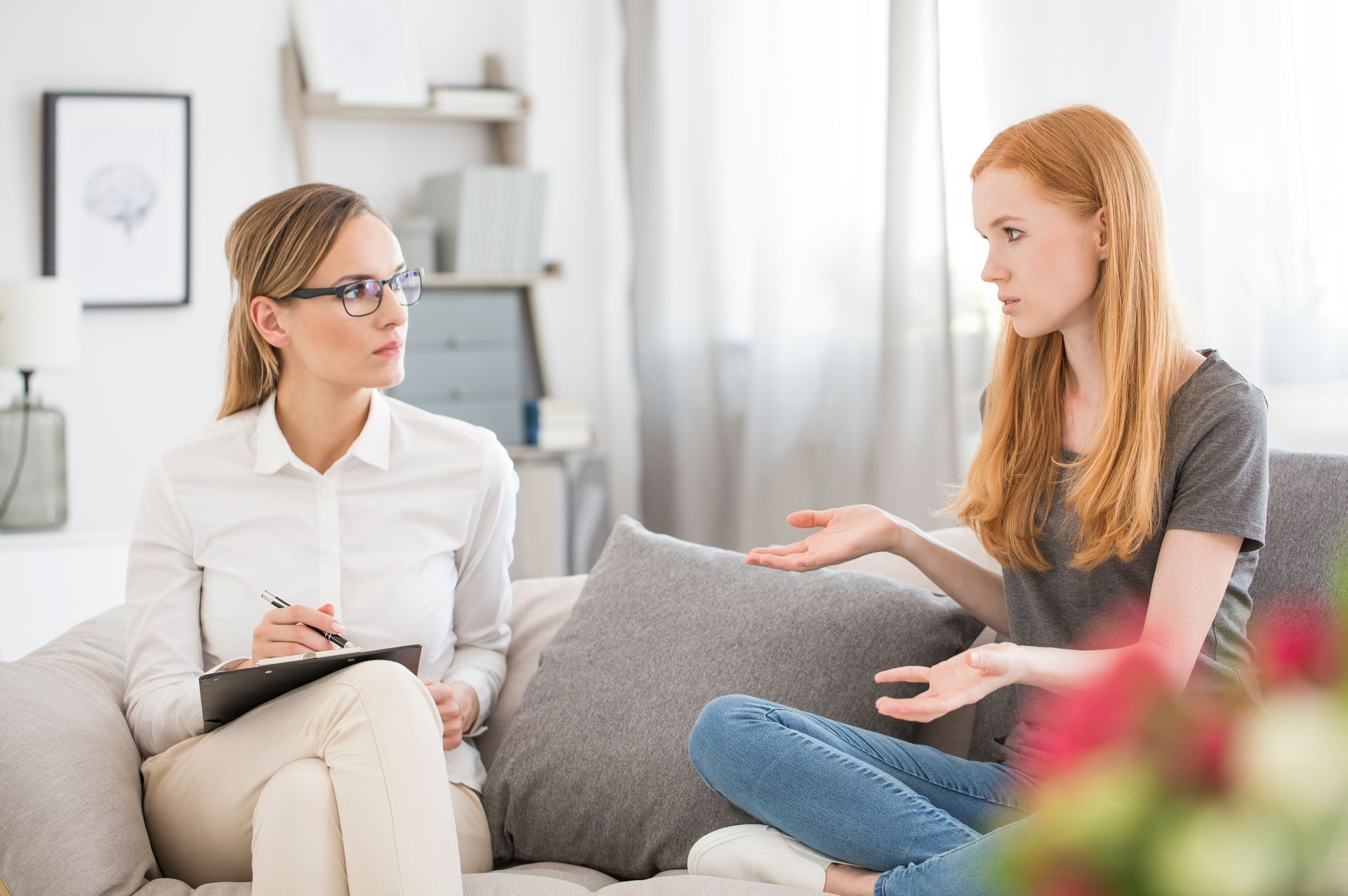 A woman with red hair gestures while talking to a therapist in a counseling session.