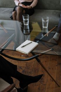 Glass coffee table with notepad and pencils in a modern living room, with two people seated nearby