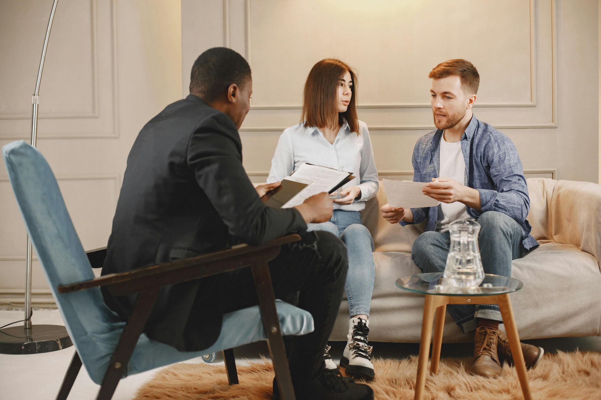 A therapist counsels a couple in a room. All three are holding papers.