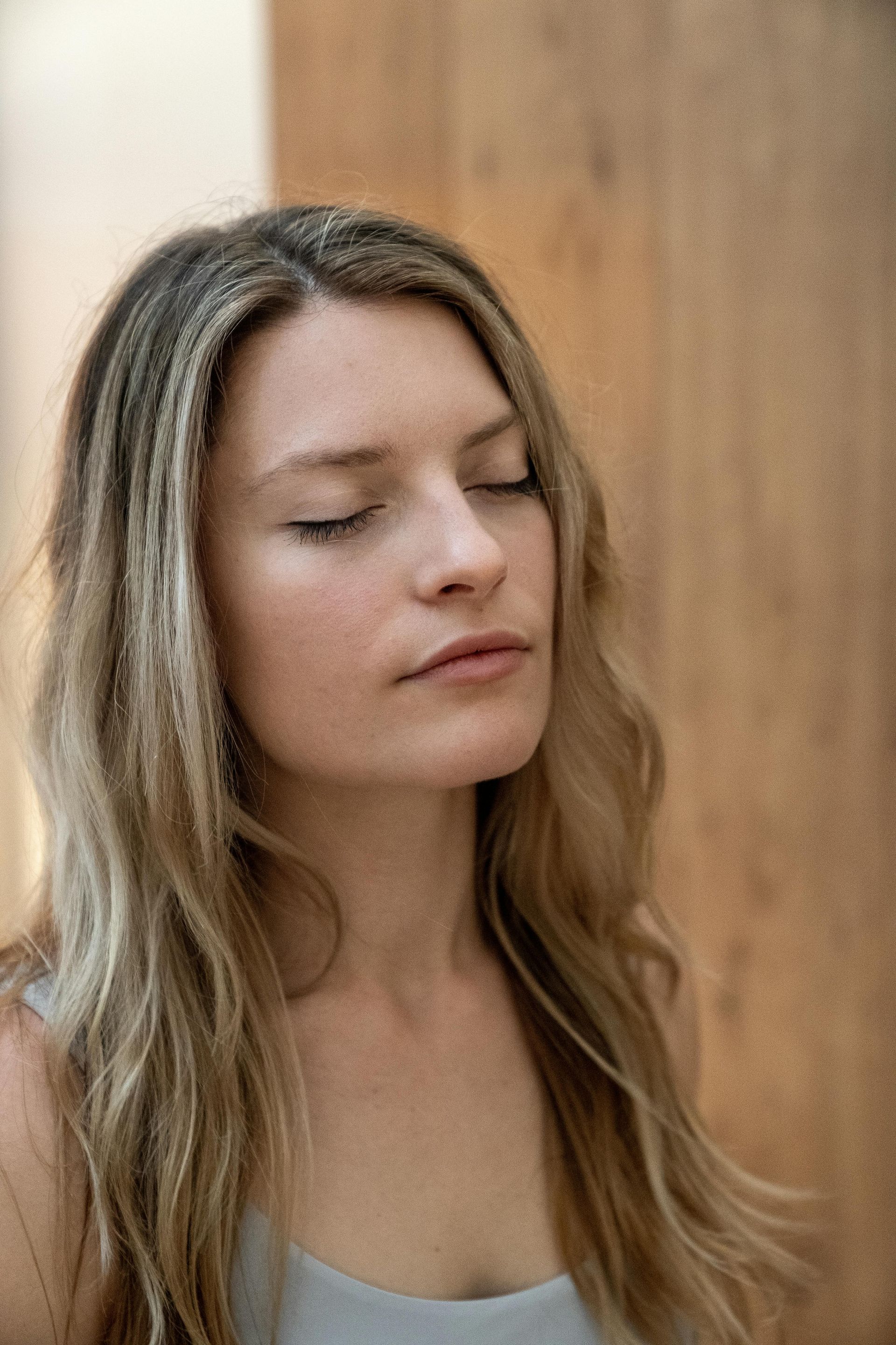 Woman with light hair and closed eyes against a wooden background.