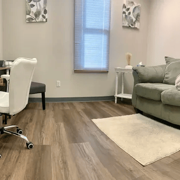 A light, modern office with a desk, chair, couch, rug, side table, and window.