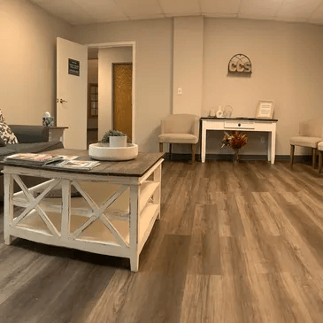 Waiting room with a white coffee table, neutral walls, and wood-look flooring.