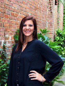 A woman in a black shirt is standing in front of a brick wall.
