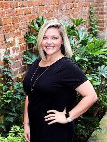 A woman in a black dress is standing in front of a brick wall.