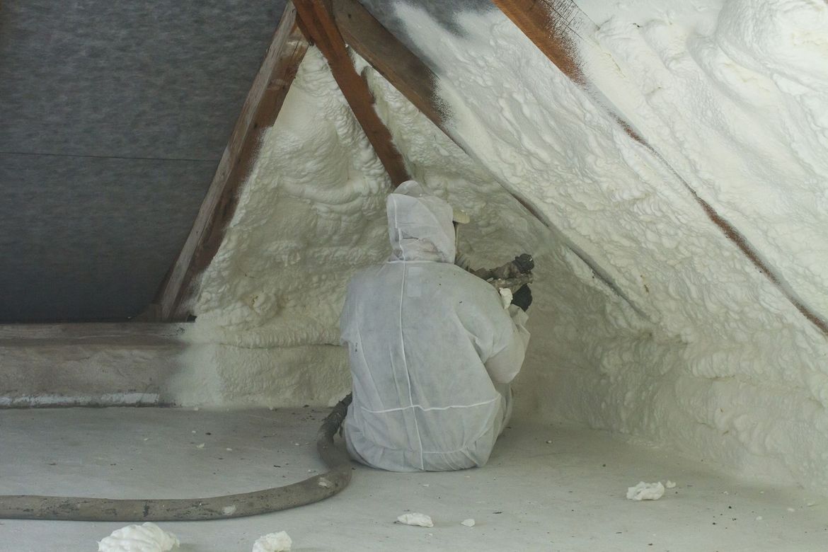 a man in a white suit is spraying foam in an attic
