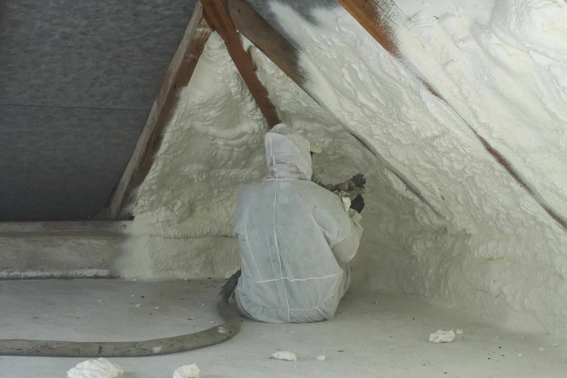 A man is spraying foam in an attic.