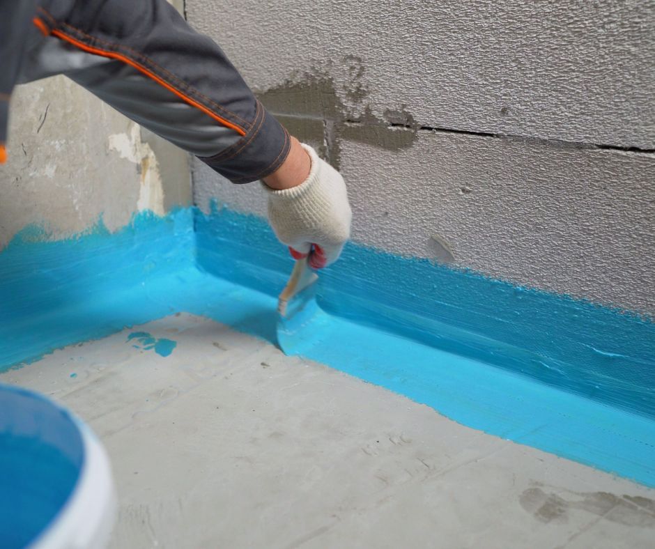 Contractor applying waterproofing membrane to a residential foundation wall.