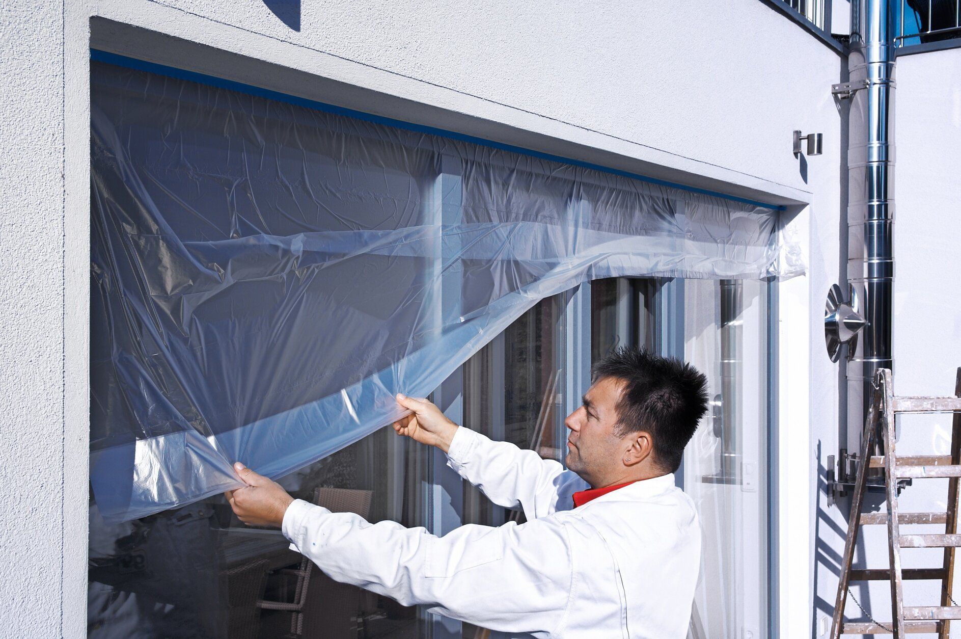 technician taping plastic sheeting to protect window frames before applying spray foam.