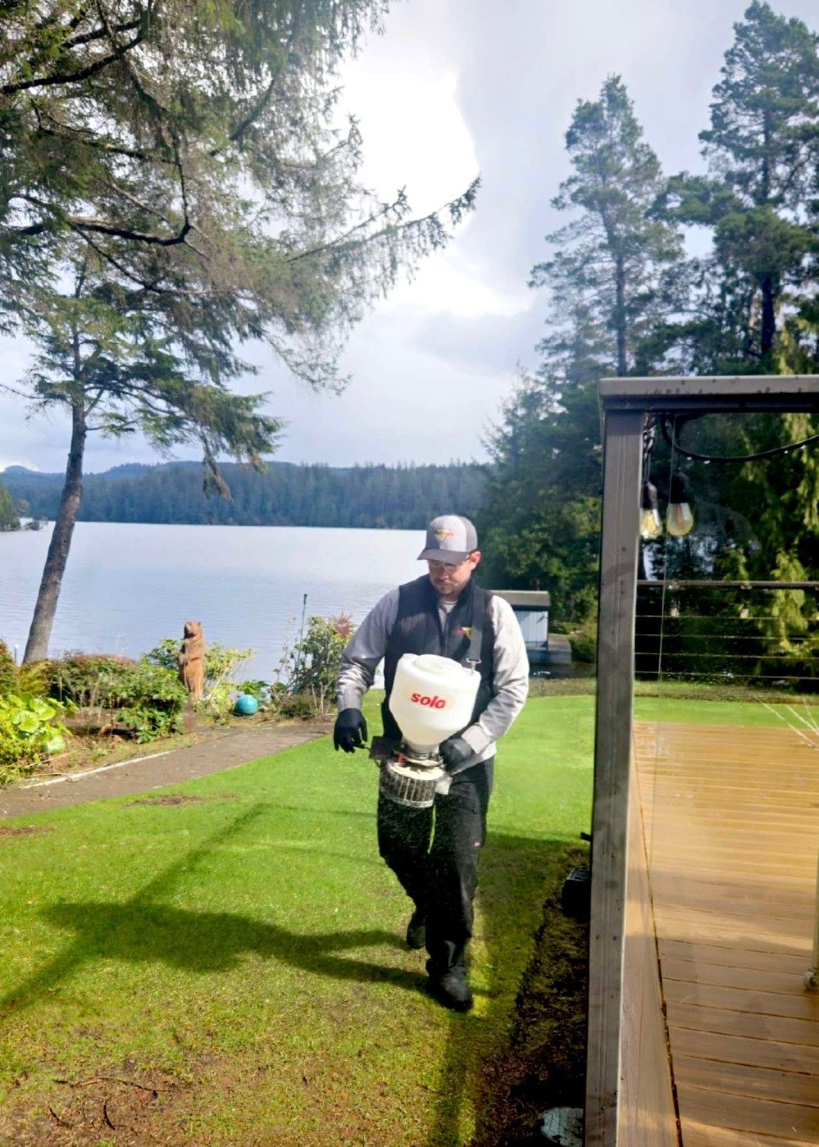 Man spreading fertilizer on lawn near lake.