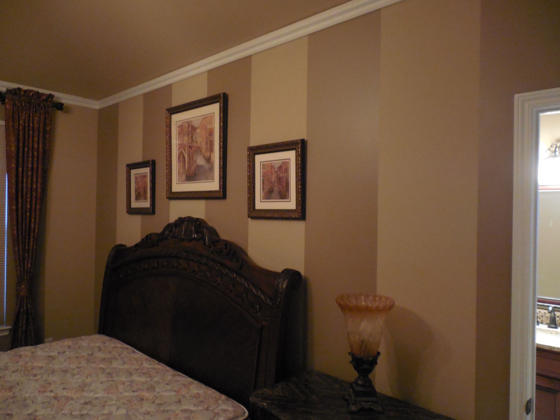 A bedroom with a bed , nightstand , lamp and striped walls.
