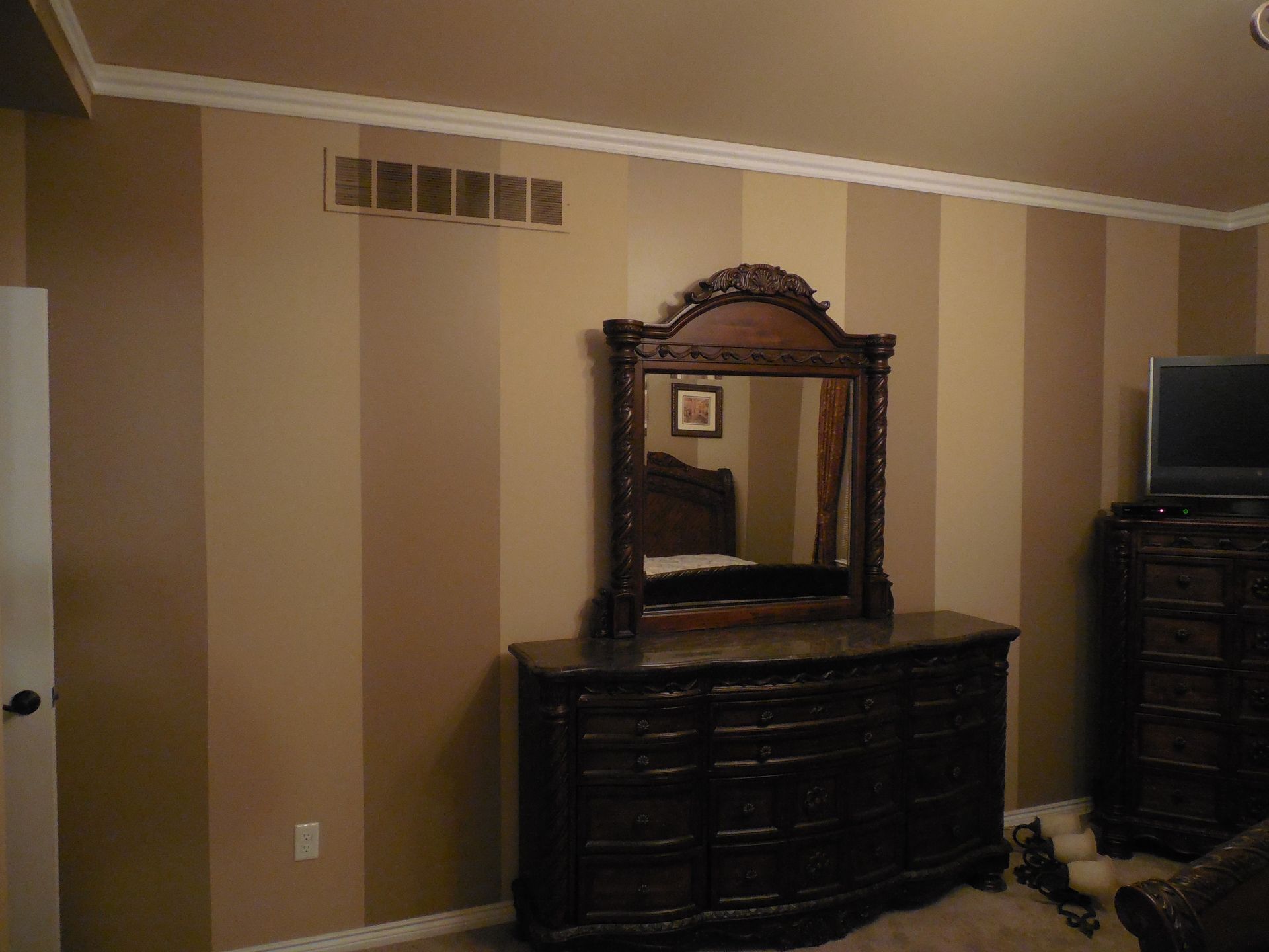 A bedroom with striped walls and a dresser with a mirror