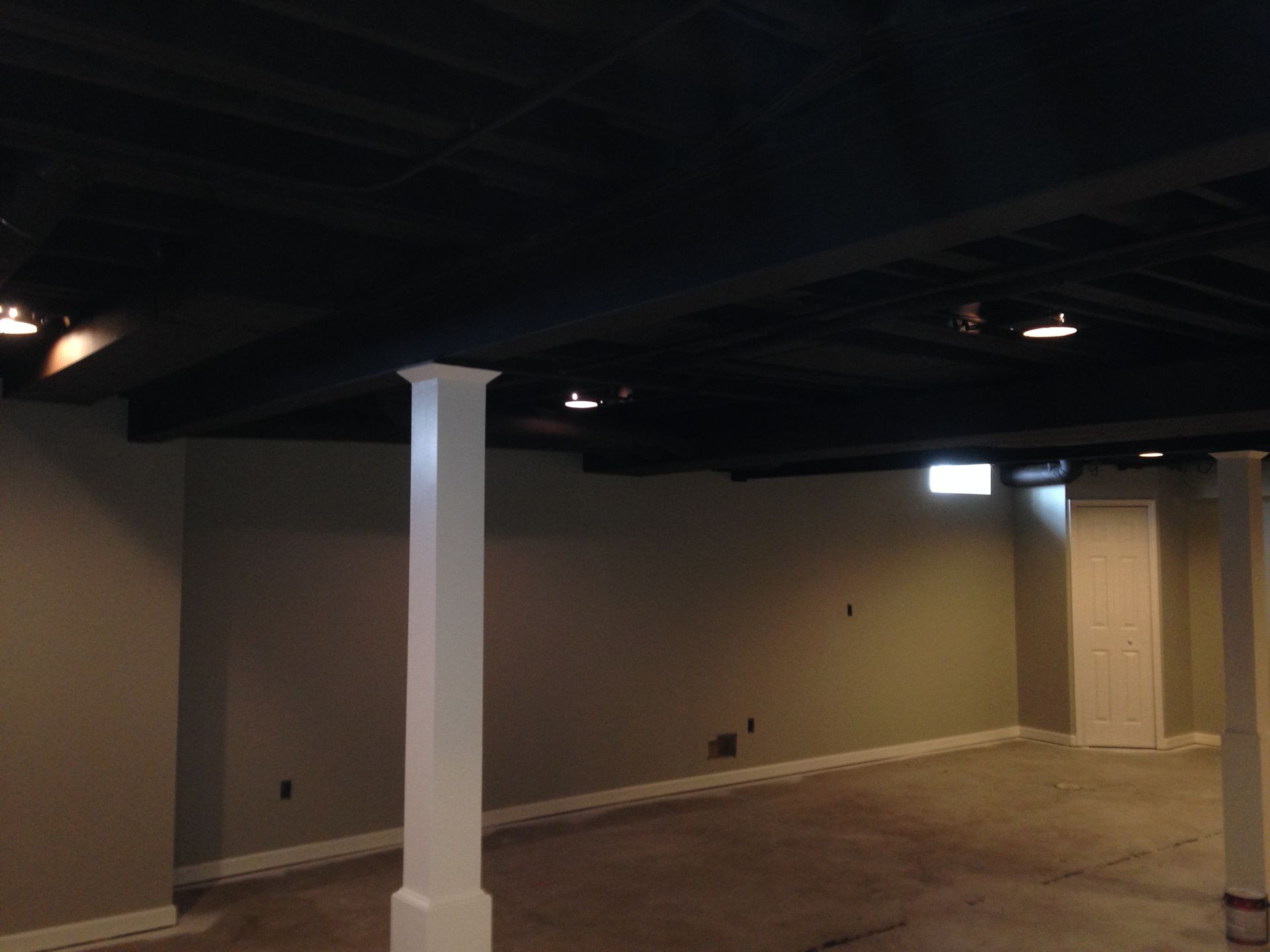 An empty basement with a black ceiling and white pillars