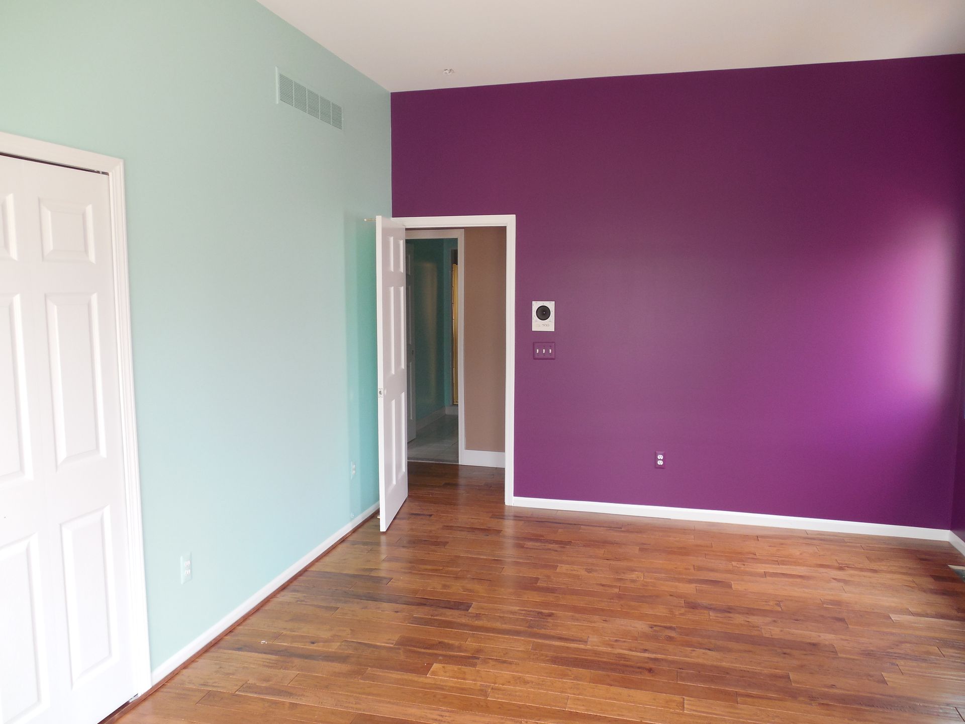 An empty room with purple and blue walls and hardwood floors.