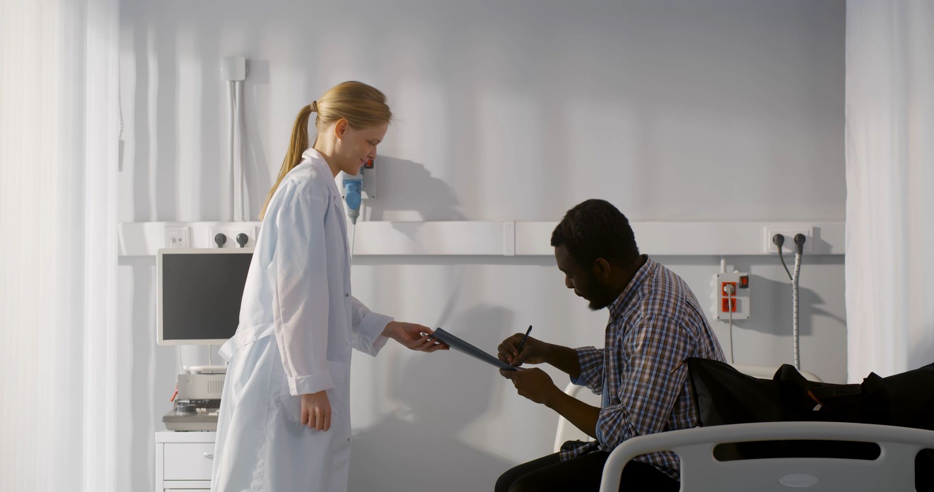 A medical professional in a white coat hands a clipboard for to a patient to be discharged