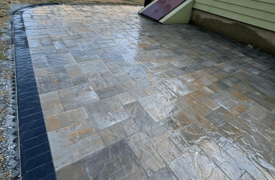 A patio with a black border is being built in front of a house.