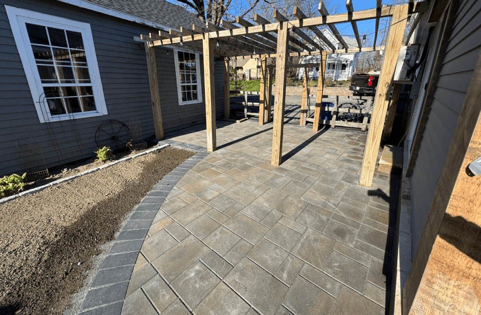 A pergola is sitting on top of a patio next to a house.