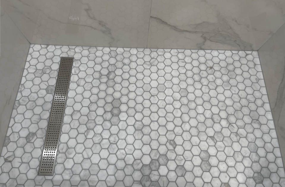 A shower with a honeycomb tile floor and a drain.