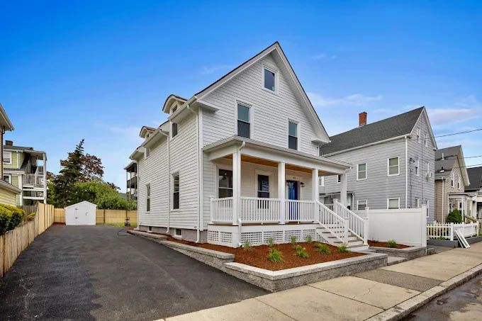 A white house with a porch and a garage is sitting on the corner of a street.