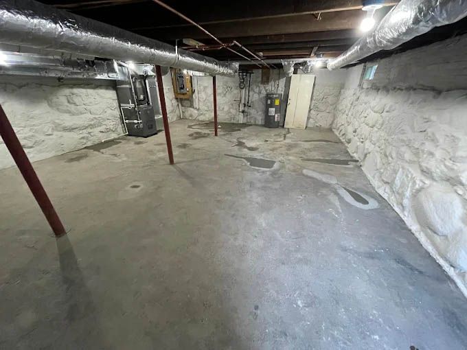 An empty basement with a stone wall and concrete floor.