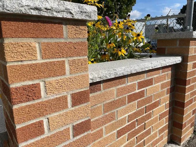A close up of a brick wall with flowers in the background.