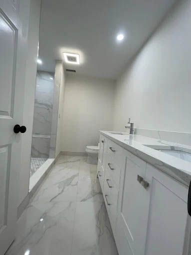 A bathroom with white cabinets , a toilet , and a walk in shower.