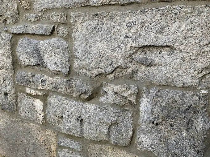 A close up of a stone wall with concrete between the bricks.